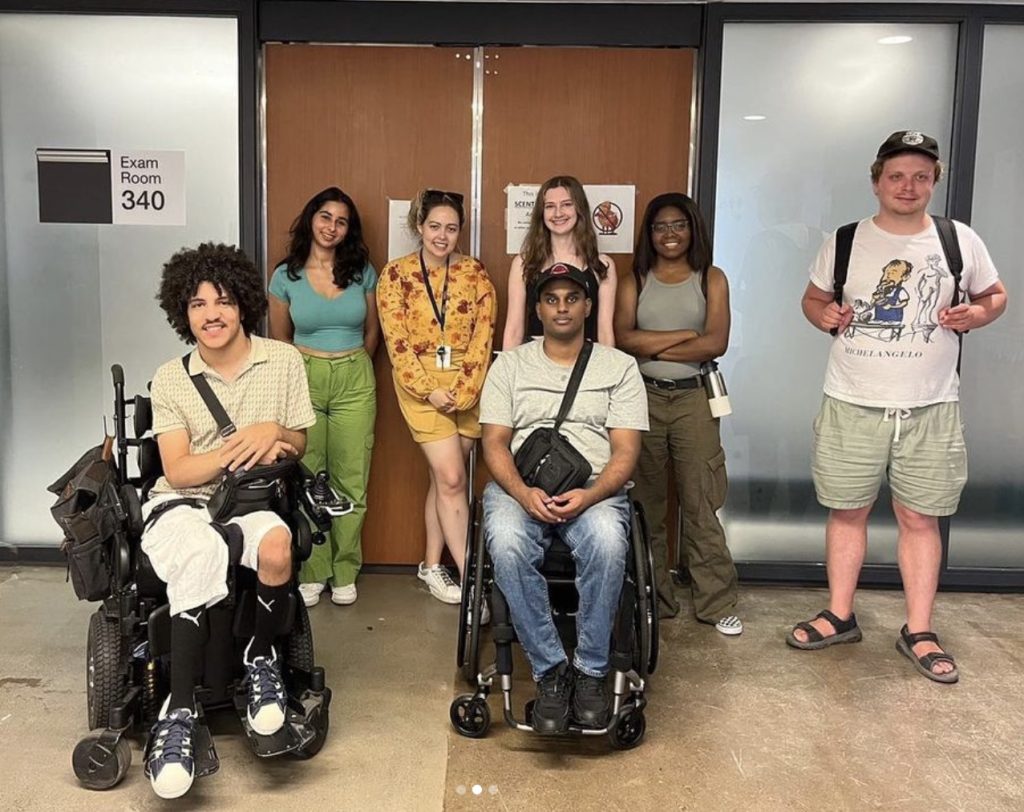 Seven students, including Catherine, smiling outside Exam Room 340 in the Exam Centre during the U-TAAC Accessibility Campus Tour.